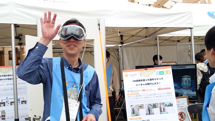 HMD（Head Mounted Display：ヘッドマウントディスプレイ）を装着し片手を挙げる男性